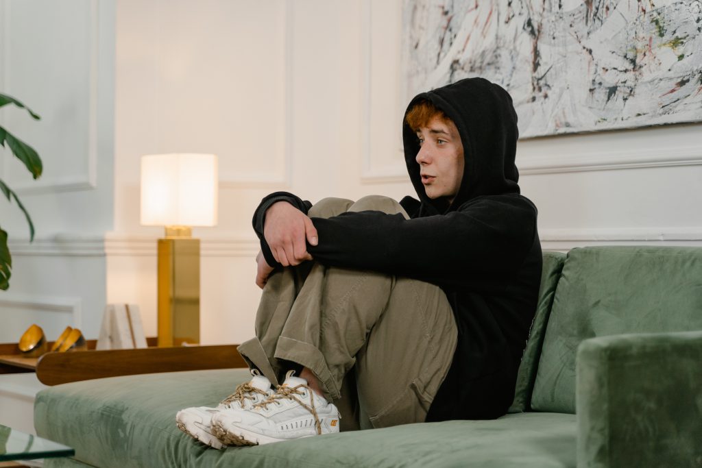 thoughtful teenager wearing a black hoodie sitting in couch