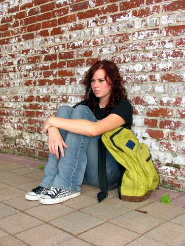 Girl with bookbag sitting against a brick wall